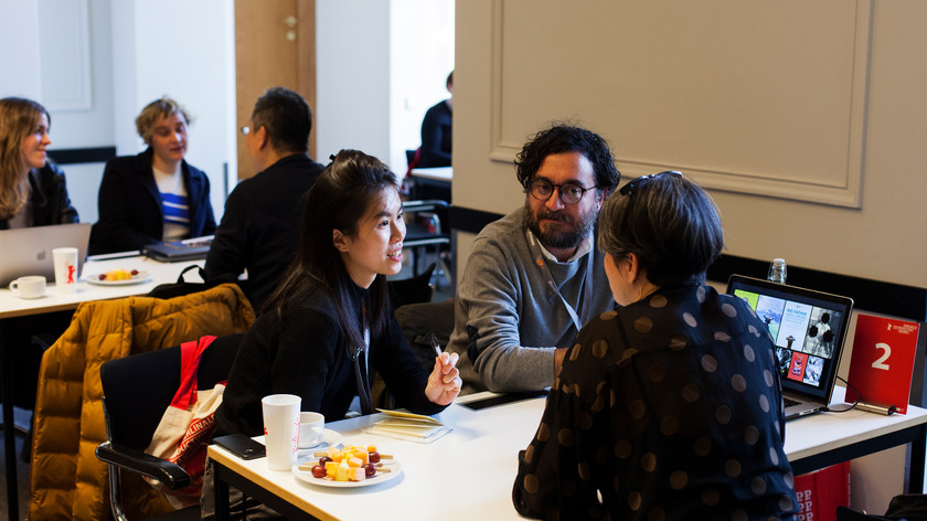 Foto. Små grupper med personer sitter rundt bord og snakker sammen.