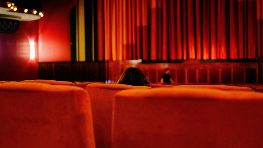 Foto. Kinosal med oransje seter. Et par personer skimtes i blidet.