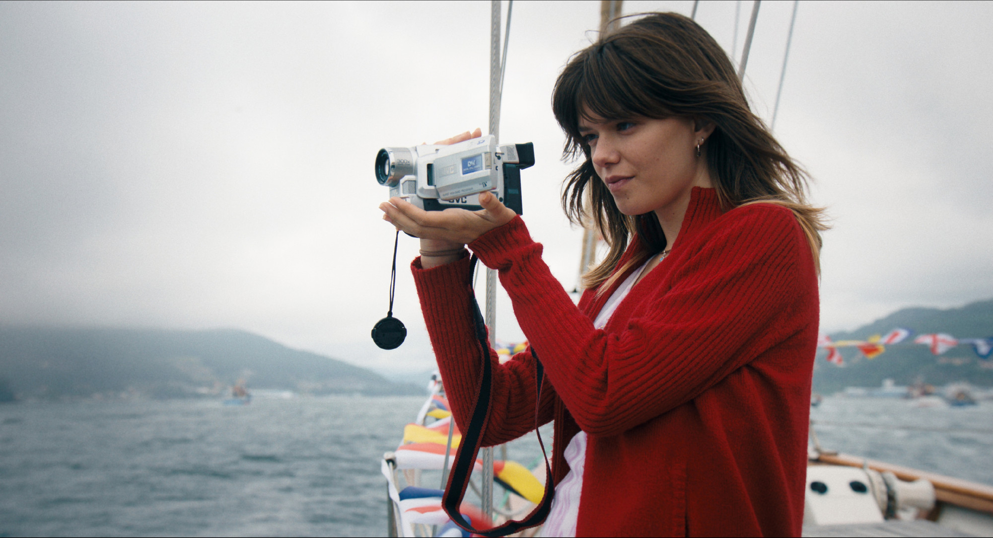 Foto. En ung kvinne holder et videokamera på en seilbåt.
