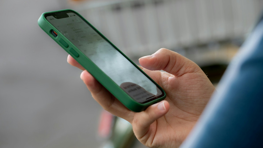 Foto. En hånd som holder en mobiltelefon med grønt etui.