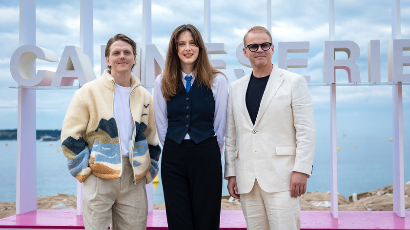 Foto. To menn og en dame poserer foran et skilt med teksten Canneseries.