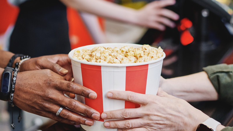 Foto. To sett hender holder en bøtte med popcorn.