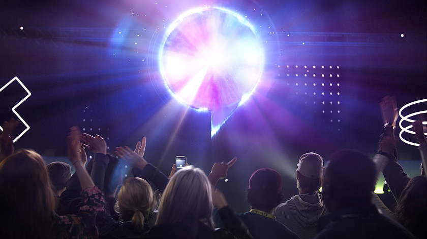 Foto. Gamescom logoen lyser i et mørkt rom hvor en mengde mennesker ser mot logoen og klapper.