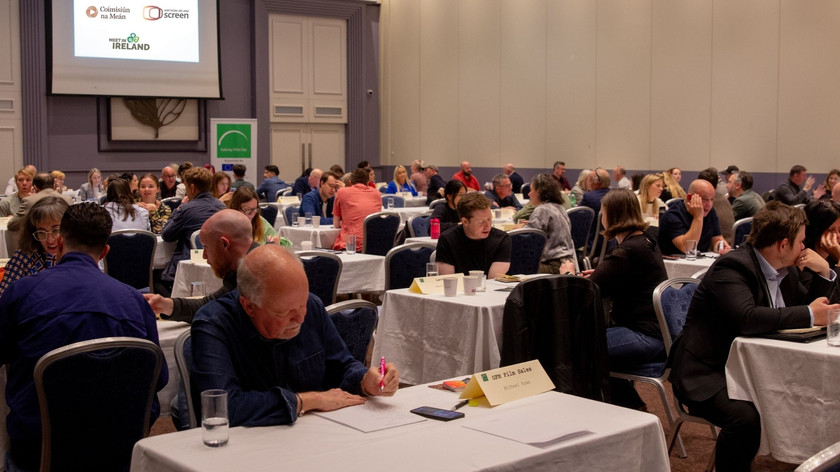 Foto. Ved ulike bord i et stort rom sitter personer og snakker sammen.