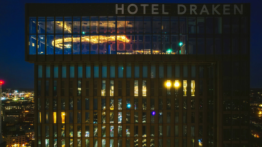 Foto. Bilde av en hotellfasade på kveden hvor omgivelsene speiles i fasaden.