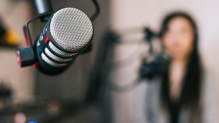 Foto. En mikrofon i et studio. I bakgrunnen skimtes en dame bak en annen mik.