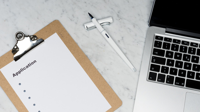 Foto. En PC, en penn og et papir ligger på et bord sett ovenfra.