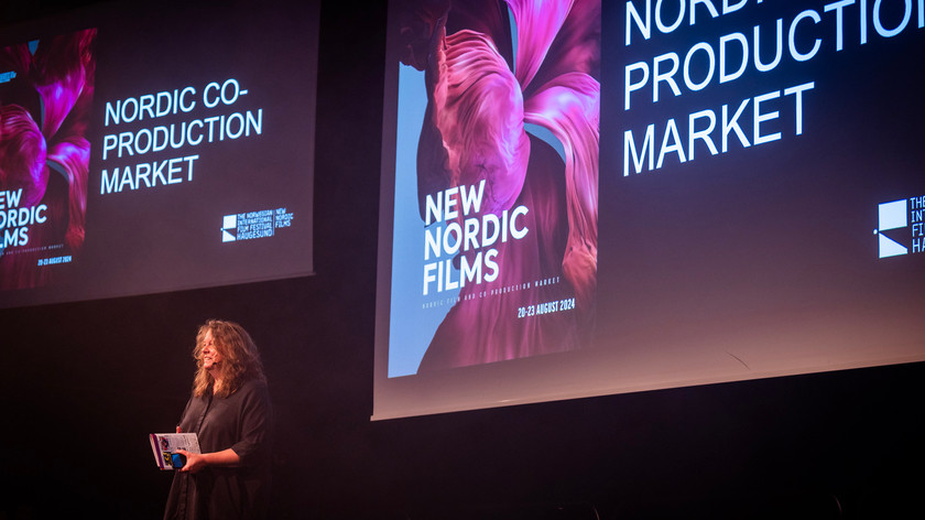 Foto. En dame står på en scene foran to store lerreter.