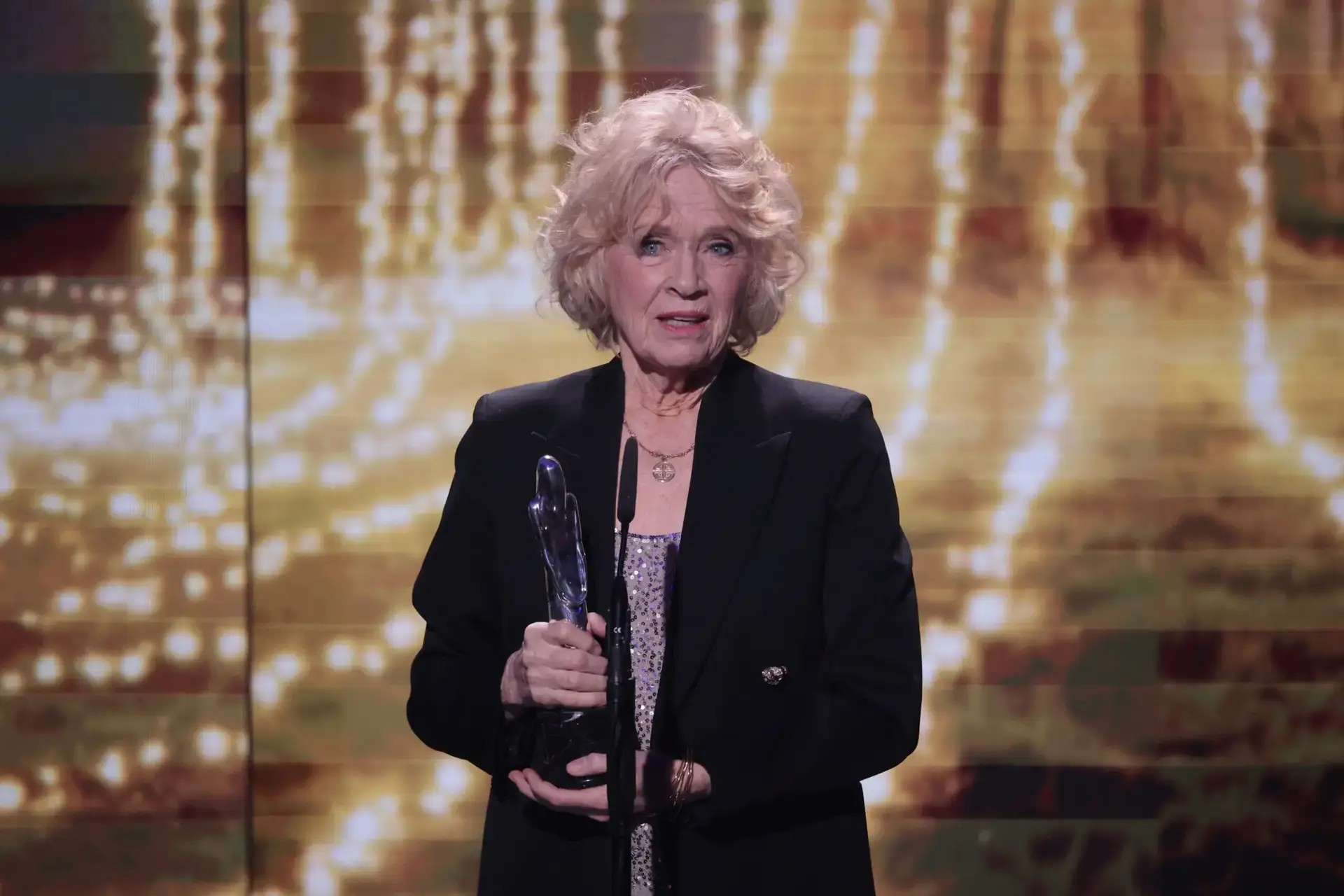 Foto. En eldre dame holder en statuett på en scene.