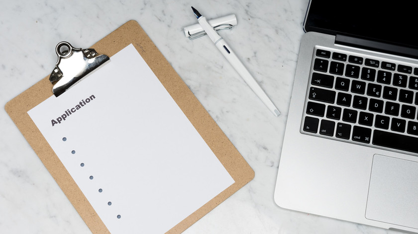 Foto. En PC, en penn og et papir ligger på et bord sett ovenfra.